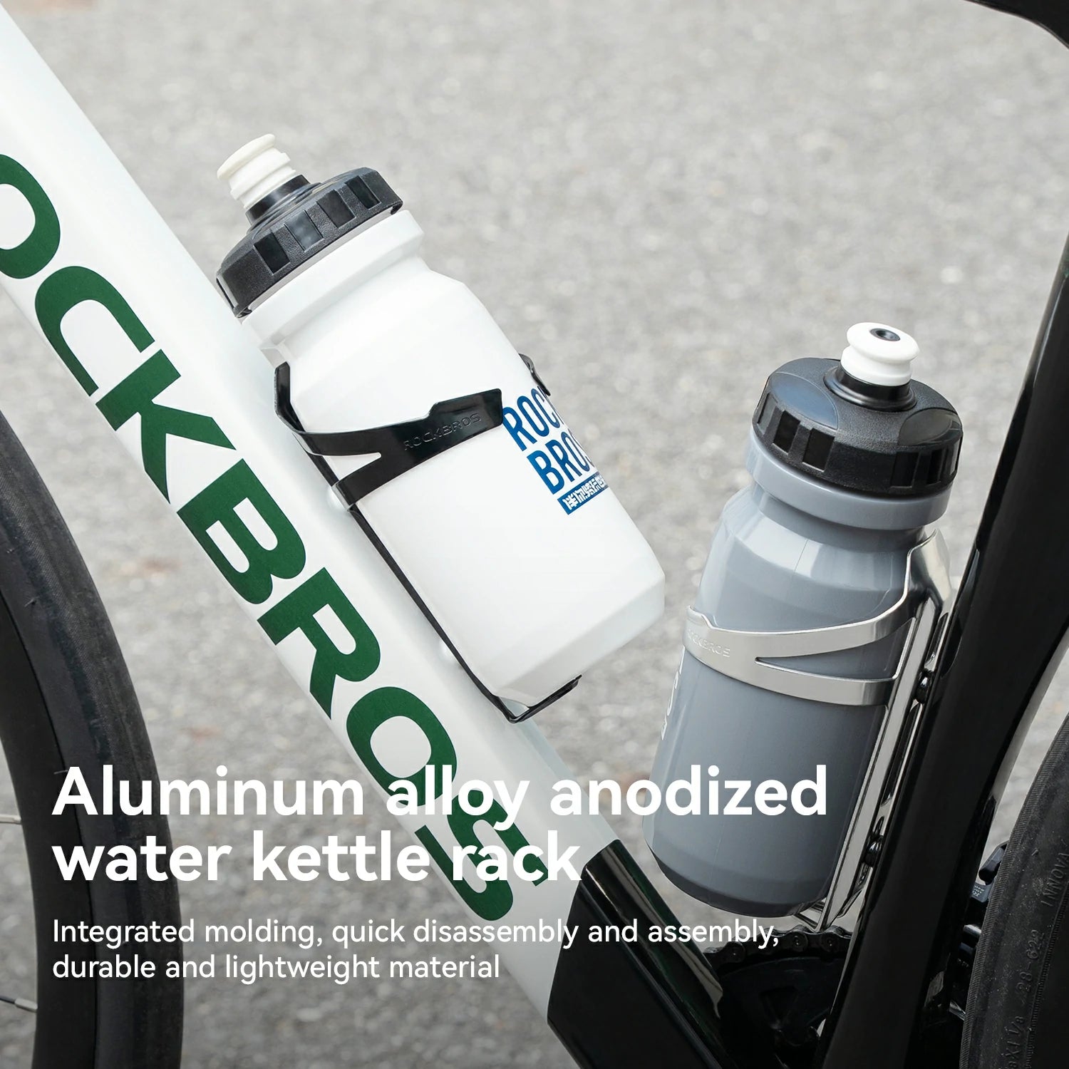 Close-up of a bicycle frame with two RockBros water bottles mounted in black and silver aluminum anodized water kettle racks. White and gray bottles are shown against a blurred gray pavement background, with descriptive text overlaid at the bottom.