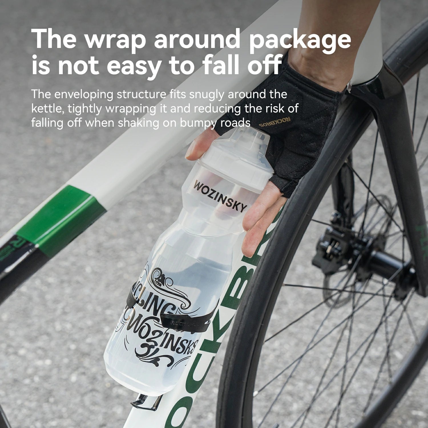 A close-up of a person's hand wearing a black cycling glove and holding a clear Wozinsky cycling bottle with a black and white label, wrapped around a road bike frame and wheel. White text at the top explains the bottle's secure wrap design.