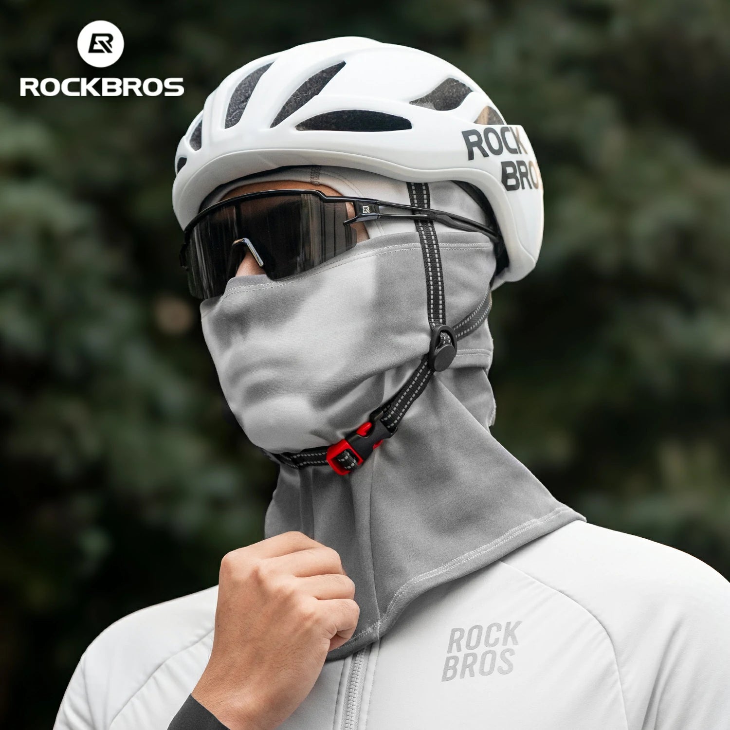 Person wearing a white helmet, gray balaclava, and white jacket with 'RockBros' branding against a blurred green background.#color_Dark Gray