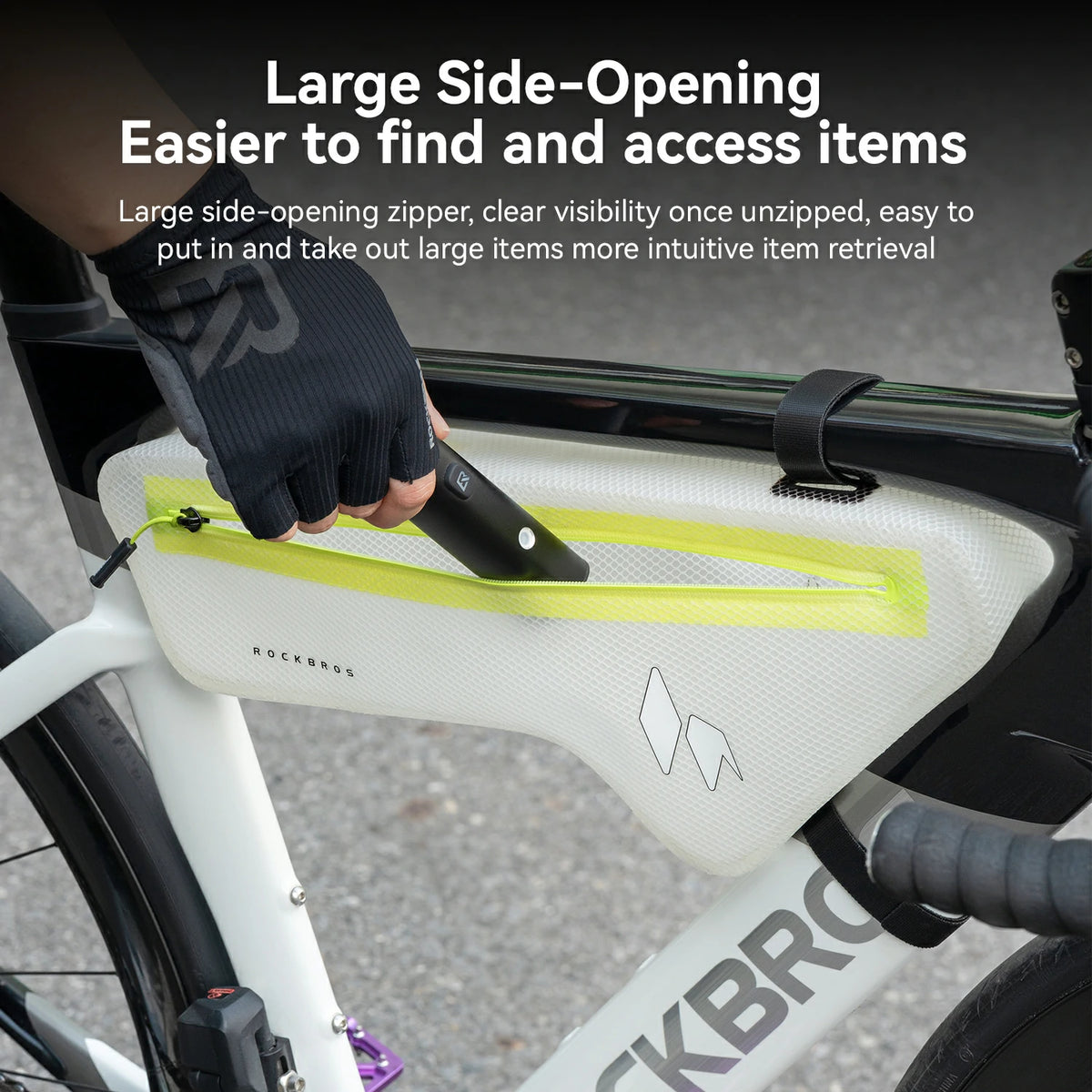 A close-up of a bicycle frame with a white RockMeat side bag featuring a bright yellow-green zipper. A gloved hand is pulling the zipper open, with promotional text at the top describing the large side-opening design.