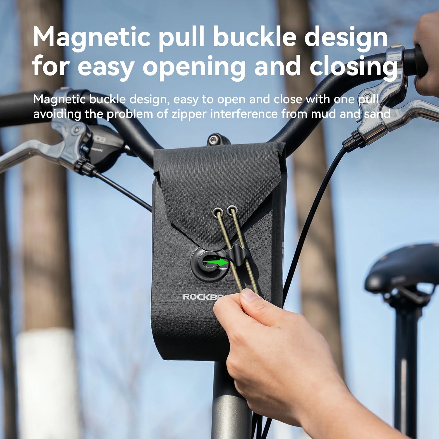 A black ROCKBROS bicycle bag mounted on a bike handlebar, with a hand demonstrating the magnetic pull buckle design. White text at the top explains the magnetic buckle feature.