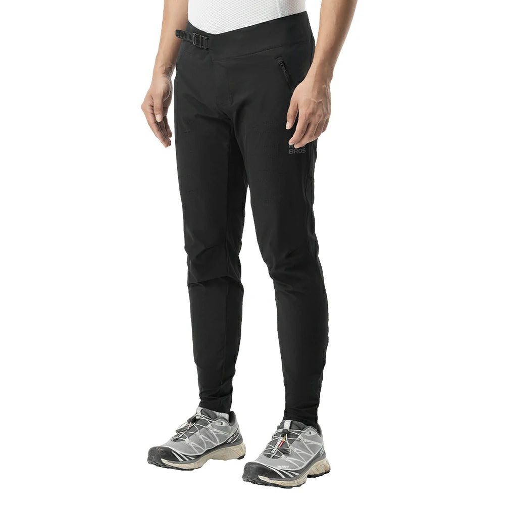 Black slim-fit hiking pants shown on a model from the waist down, paired with gray and black trail running shoes against a plain white background.