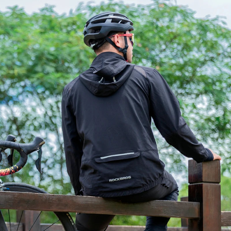 Person wearing a black jacket with 'RockBros' branding, sitting on a wooden bench with a blurred green background.