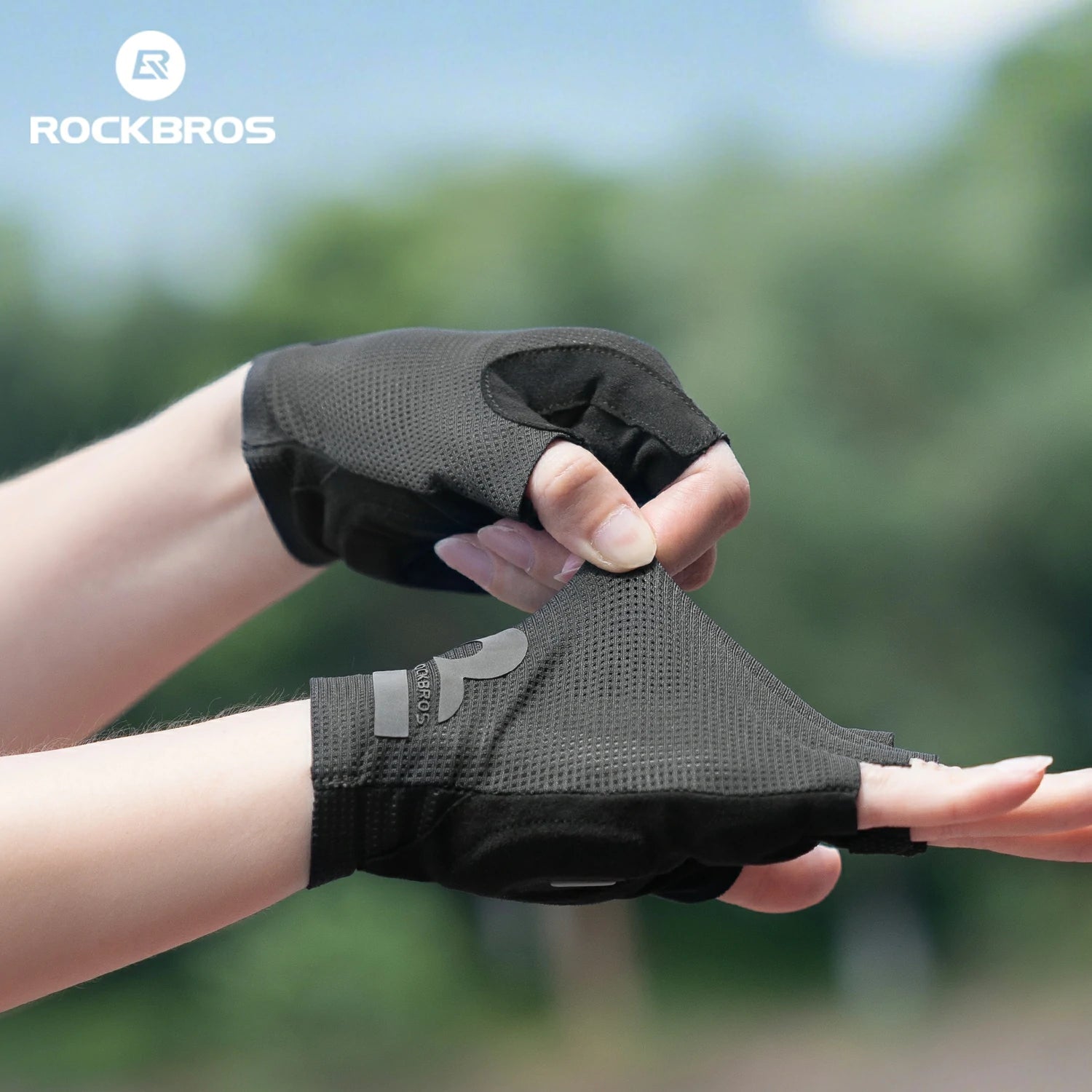 Black gloves being held with a blurred green background and 'RockBros' logo. #color_black