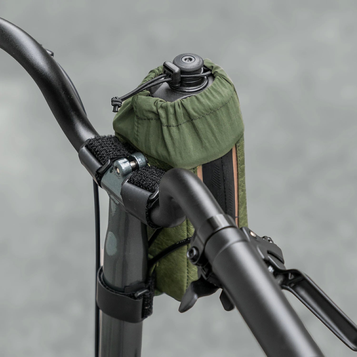 Green bag attached to a bicycle handlebar with a blurred gray background