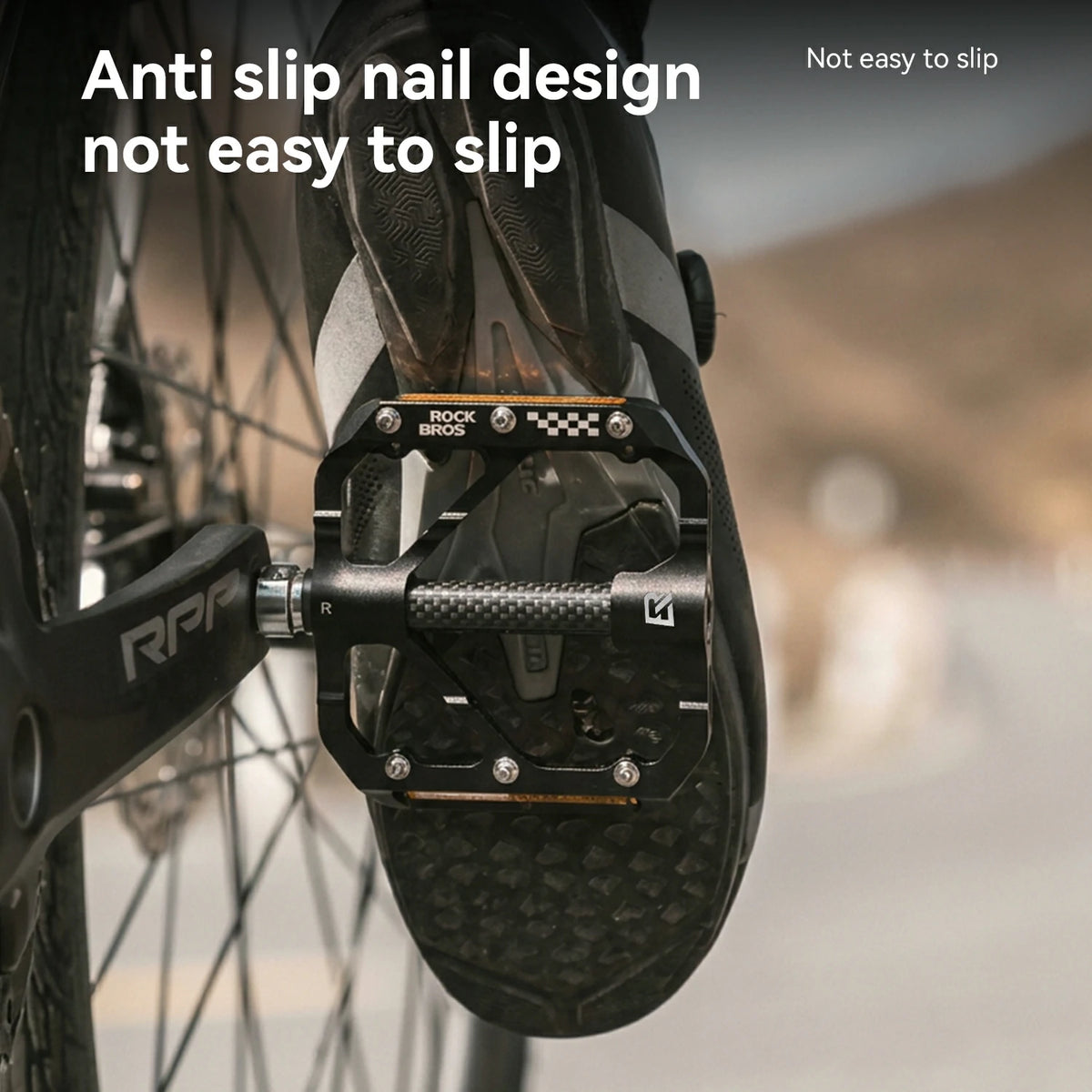 Close-up of a bicycle pedal with a black anti-slip nail design and textured tread, shown attached to a shoe on a blurred outdoor road background. White text reads 'Anti slip nail design not easy to slip' and 'Not easy to slip'.