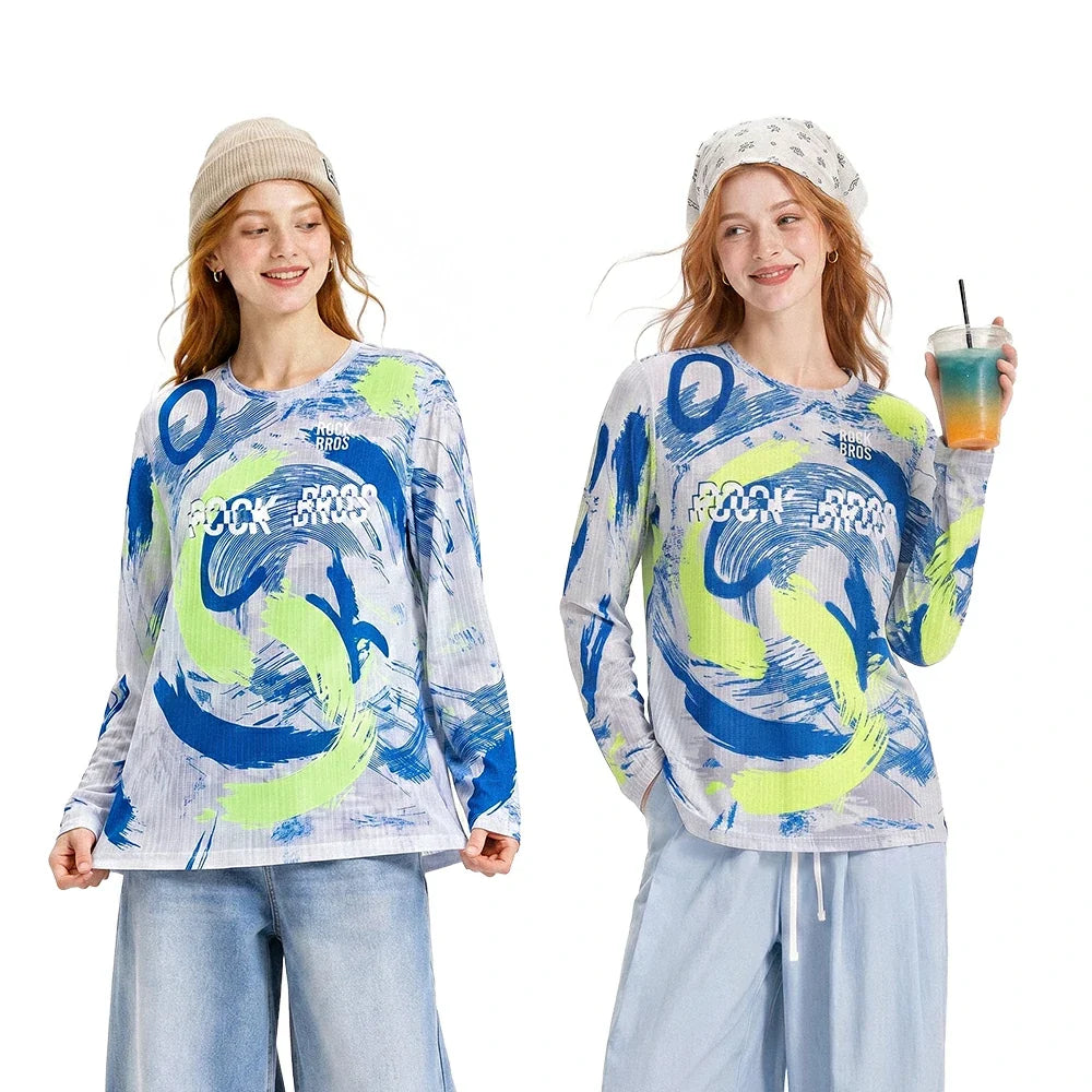 Two women modeling matching long-sleeve graphic shirts with a blue, neon yellow-green, and white abstract print and the words 'ROCK A DROPS'. The left model wears a beige beanie and light blue jeans, while the right model wears a white patterned beanie, light blue jeans, and holds an iced drink.
