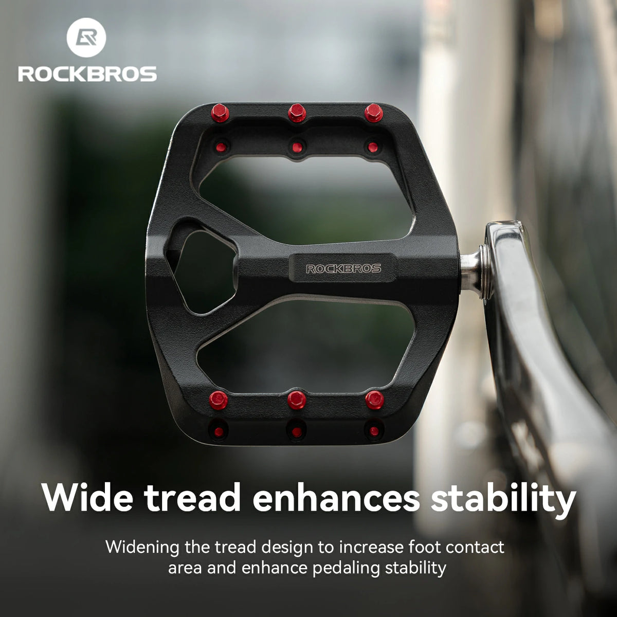 A black Rockbros bicycle pedal with red pivot pins, shown in a close-up with marketing text and the Rockbros logo on a blurred outdoor background.