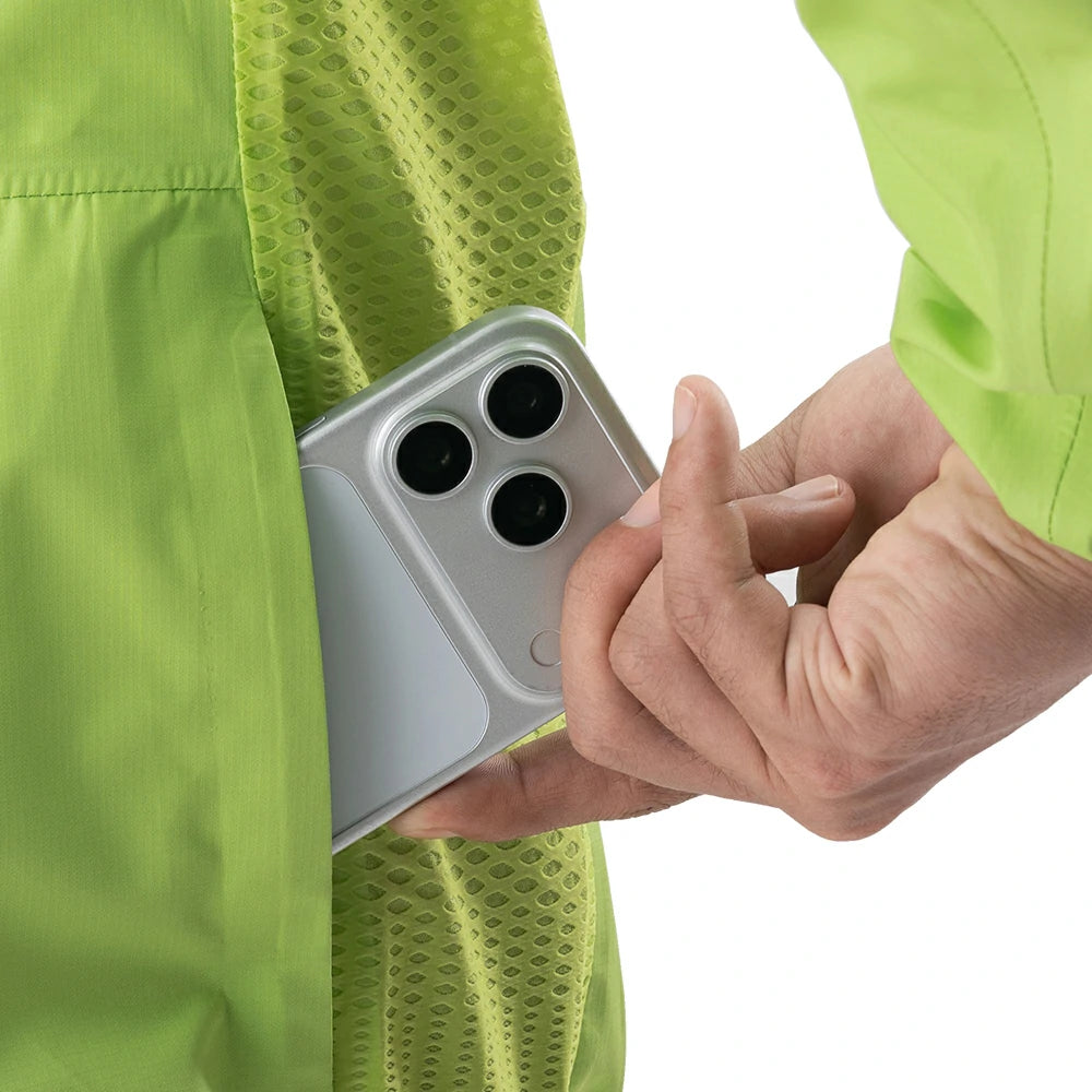 A close-up of a person wearing a bright lime green mesh jacket or vest, with a hand sliding a silver smartphone into the side pocket.
