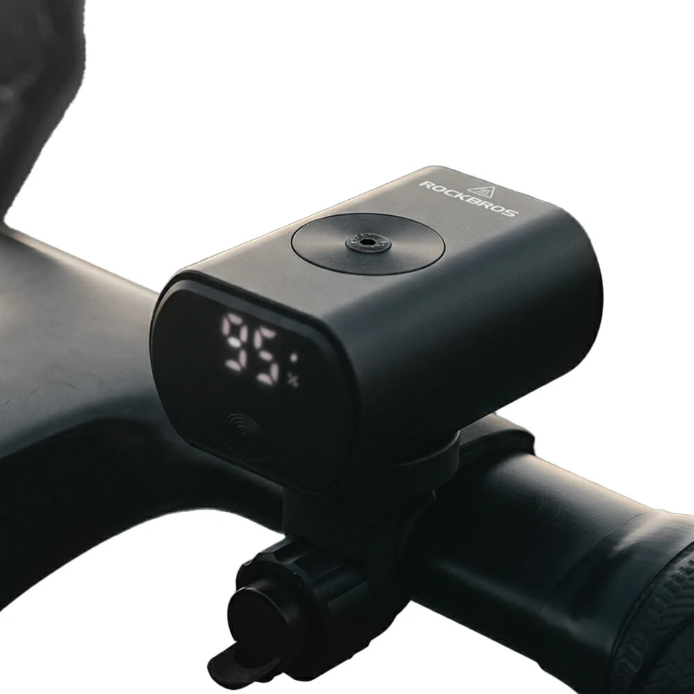 A black ROCKBROS bicycle handlebar-mounted clock and alarm device with a digital LED display showing 95:55, attached to a dark bicycle handlebar against a white background.
