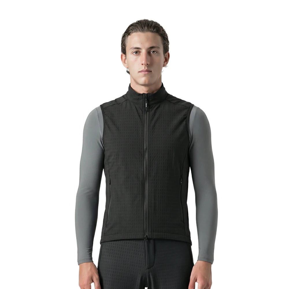 A man wearing a black zip-up athletic vest over gray long-sleeve compression sleeves, photographed against a plain white studio background.