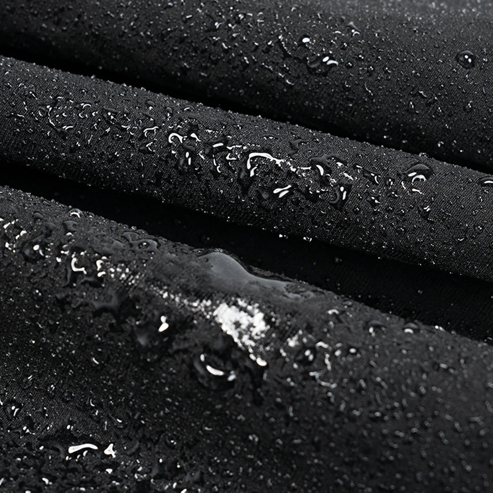Close-up of a black waterproof fabric surface with water droplets beaded on top, showing the material texture and water-repellent finish.
