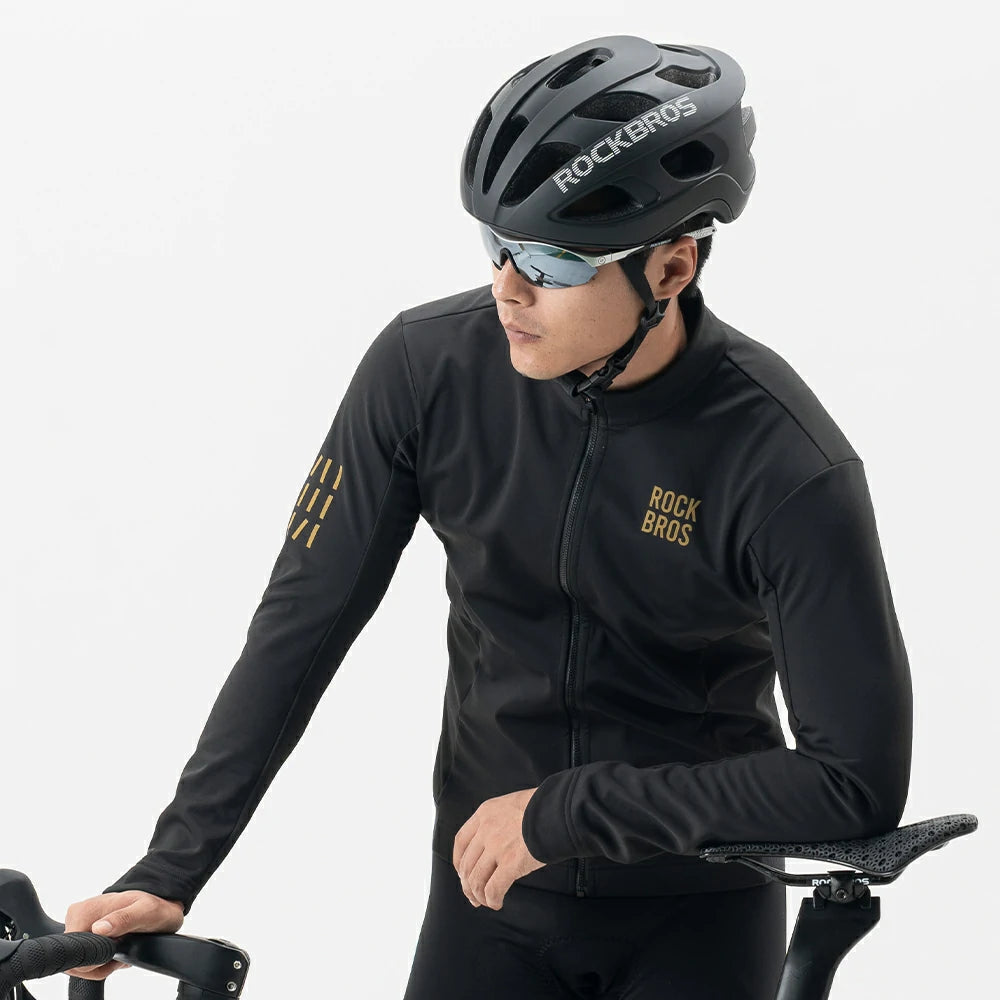 A man wearing a black Rock Bros cycling jersey, black Rock Bros helmet, and sunglasses, leaning on a bicycle against a light gray background.