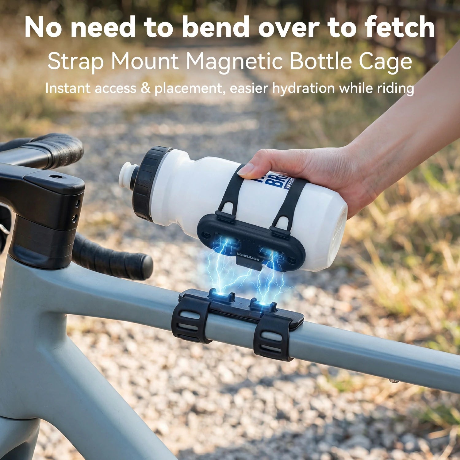 A white water bottle with a black cap is being held by a hand using a black magnetic bottle cage mounted on a gray bicycle frame outdoors. Large text at the top reads 'No need to bend over to fetch Strap Mount Magnetic Bottle Cage Instant access & placement, easier hydration while riding.