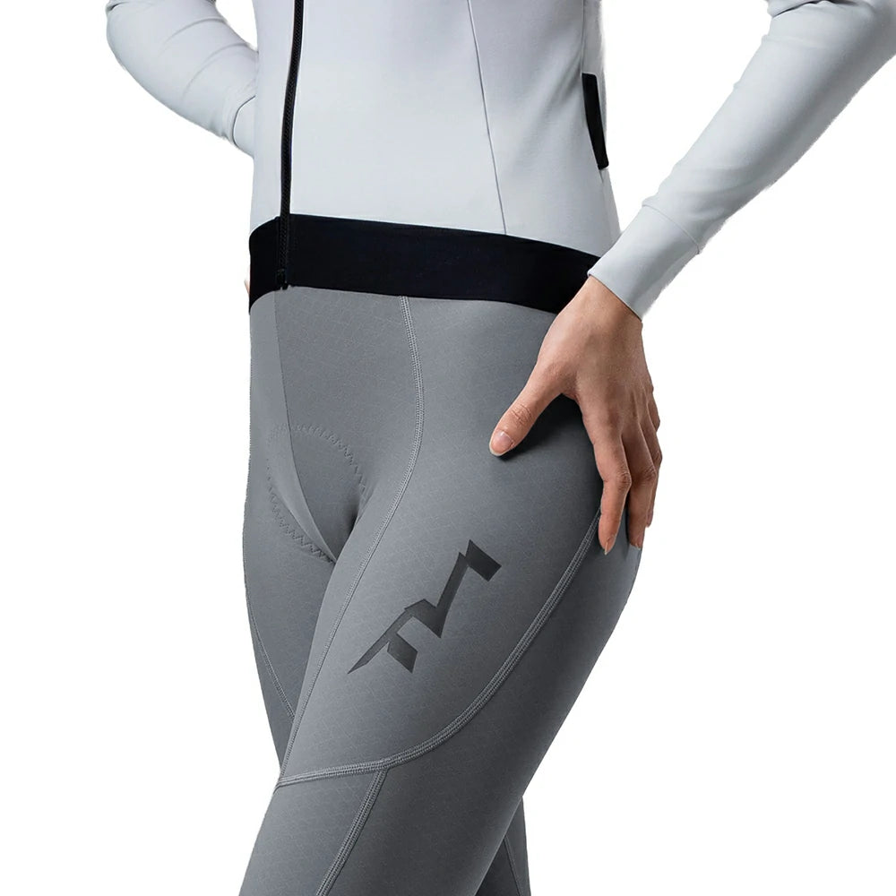 A close-up of a model wearing gray athletic cycling tights with a dark gray logo on the thigh, paired with a white and black cycling jersey against a white background.